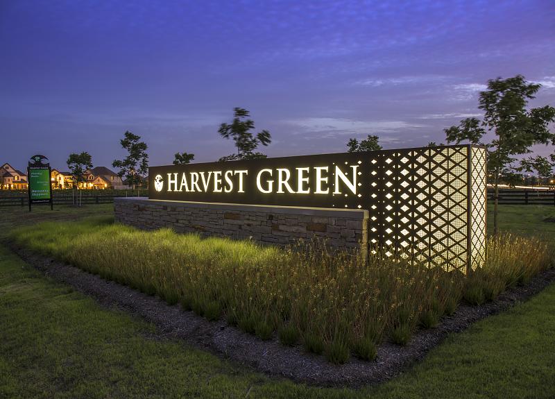 A twilight photo of Harvest Green's lit up welcome monument and landscaping.