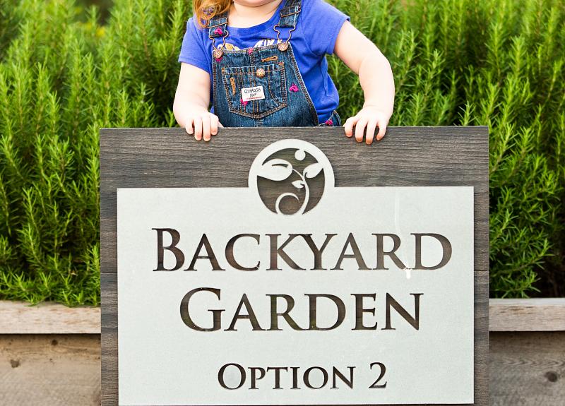 A girl behind the sign for a Backyard Garden  in Harvest Green.