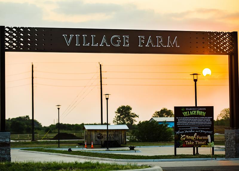 A sunset view of Village Farm sign in Harvest Green, Fort Bend.