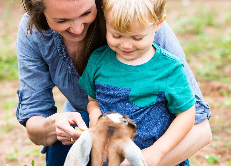 Little boy and mom play with goats, their neighbors in Harvest Green.